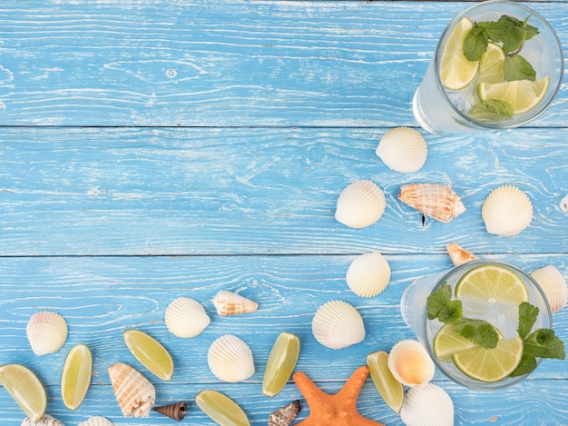 A refreshing summer drink with lime and mint Mojito stands on blue boards with seashells and starfish. Top view, copy space.