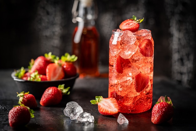 Refreshing summer drink with strawberry and ice in a glass on dark background