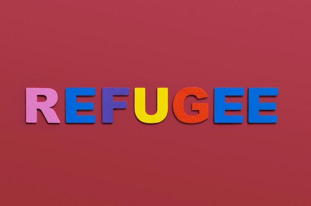 Refugees word written in colorful wooden alphabet letters on red background Safe migration for people escaping from war support and assistance concept Top view Copy space