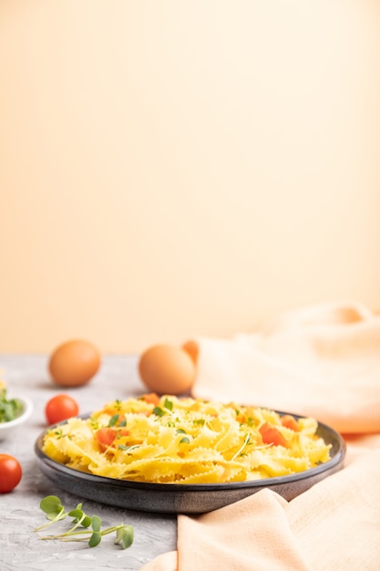 Reginelle semolina pasta with tomato, eggs and microgreen sprouts on a gray and orange background. Side view, selective focus.