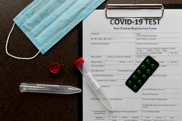 Registration form for coronavirus and two blood tubes with mask and pills lyingsurface