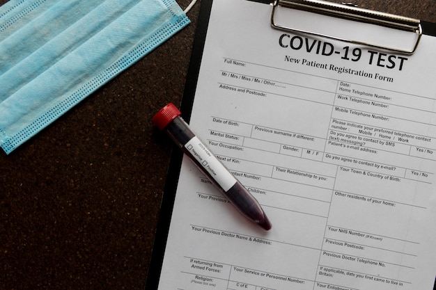 Registration form for coronavirus with a full blood tube and a  face mask lyingsurface