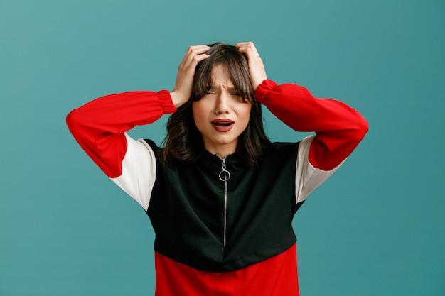 Regretful young caucasian woman keeping hands on head looking at camera isolated on blue background