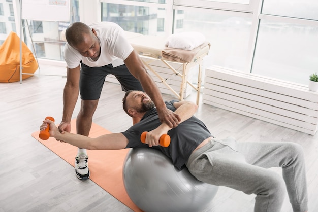 Rehabilitation center. Serious skilled coach working with a patient while being in the rehabilitation center