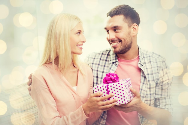 relationships, love, people, birthday and valentines day concept - happy man giving woman gift box over holidays lights background