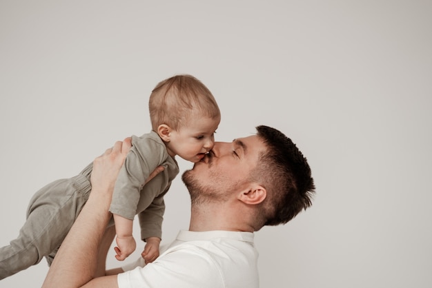 A relative of a small child is happy with their first meeting, kisses the baby on the cheek, holding high in his arms, a photo taken in a bright room on a white background