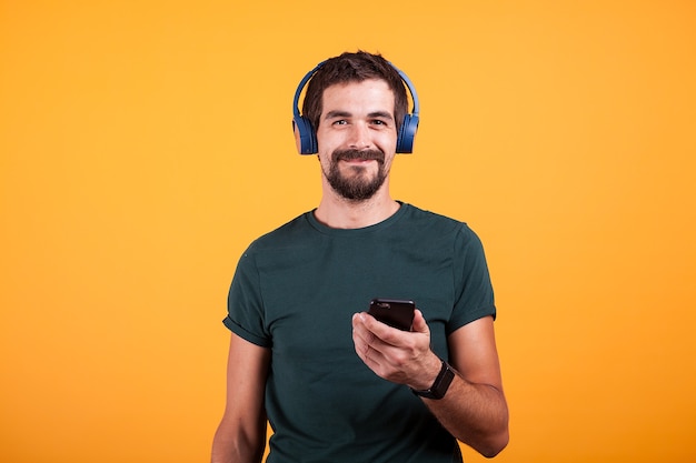 Relax attractive man with blue headphones and smartphone in his hands on orange background in studio