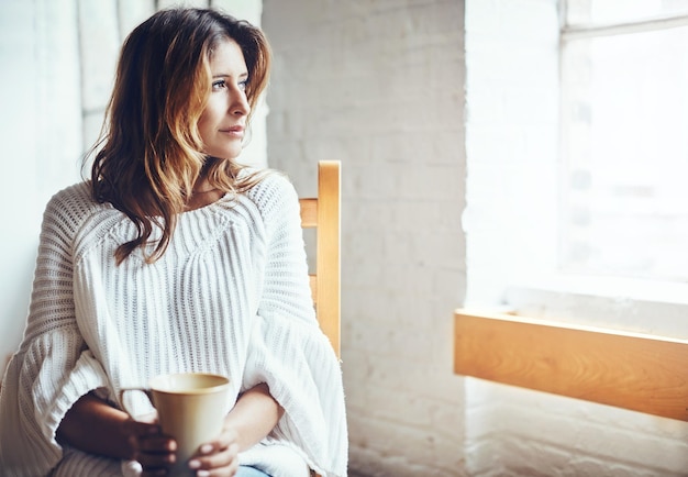 Relax thinking and woman drinking coffee in her home content and quiet while daydreaming on wall background Tea comfort and calm female enjoying peaceful morning indoors while looking out window