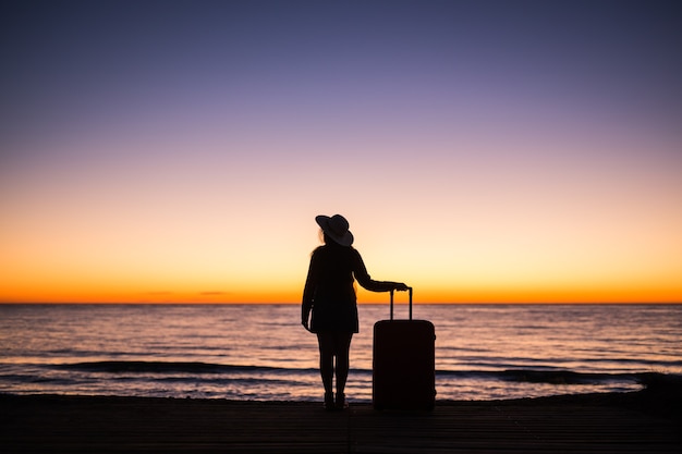 Photo relax woman with suitcase on a beach at sunset silhouette. holiday travel concept. young lady with suitcase on ocean landscape.