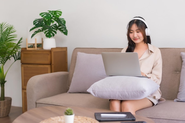 Relaxation lifestyle concept Young Asian woman is wearing headphone and watching movie on laptop