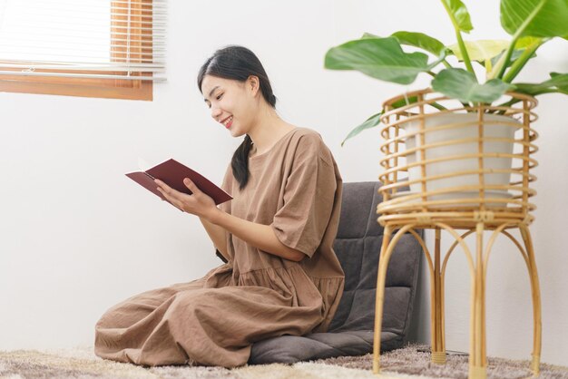 Relaxation lifestyle concept Young Asian woman reading book while sitting to relax in living room