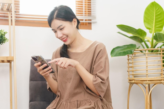 Relaxation lifestyle concept Young Asian woman use smartphone to surf social media in living room