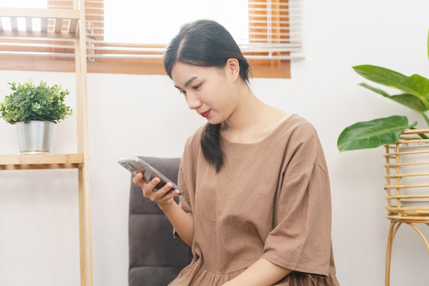 Relaxation lifestyle concept Young Asian woman use smartphone to surf social media in living room