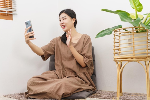 Relaxation lifestyle concept Young Asian woman using smartphone to video call beside plant pot