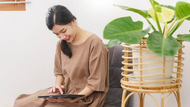 Relaxation lifestyle concept Young Asian woman using tablet to surf social media in living room