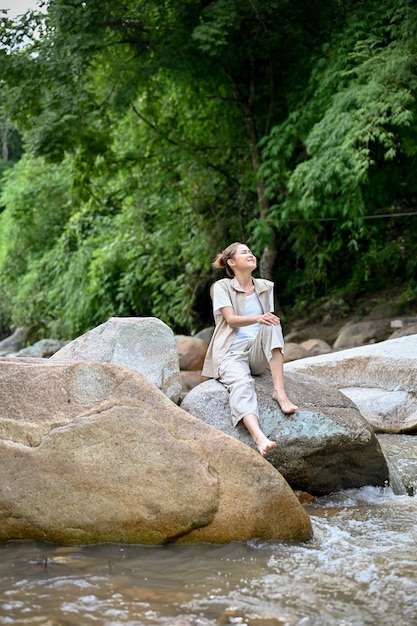 Relaxed Asian female sitting near the river on the river stone getting some fresh air camping