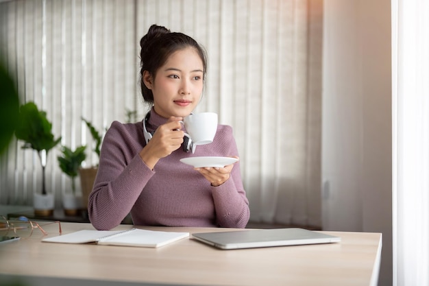 A relaxed Asian woman is daydreaming while having her morning coffee calmly at a home