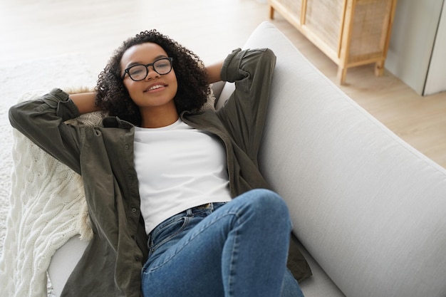 Relaxed biracial teen girl in glasses rest lying on couch enjoy break on sunny weekend at home