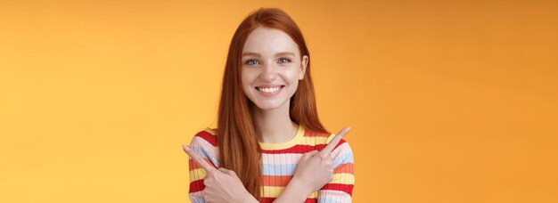 Relaxed carefree confident young helpful redhead girl showing you choices pointing crossed arms left