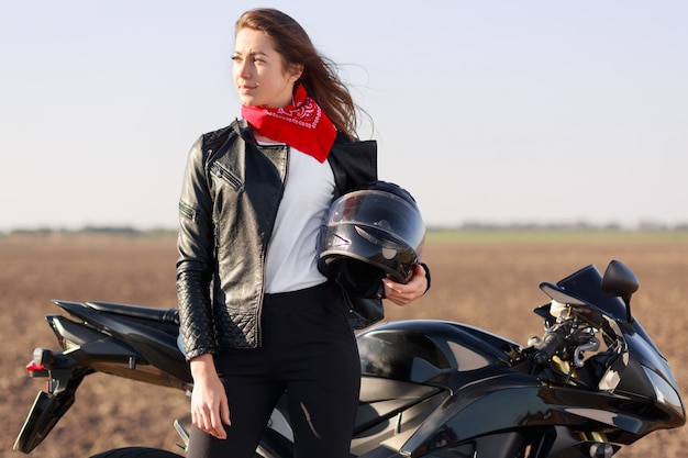 Relaxed carefree female biker looks thoughtfully aside