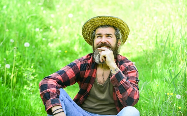 Relaxed farmer in straw hat. mature man gardener relax on green grass. enjoy spring nature. summer season in perfect. brutal ranch hipster wear checkered shirt. farming and agriculture. Green life.