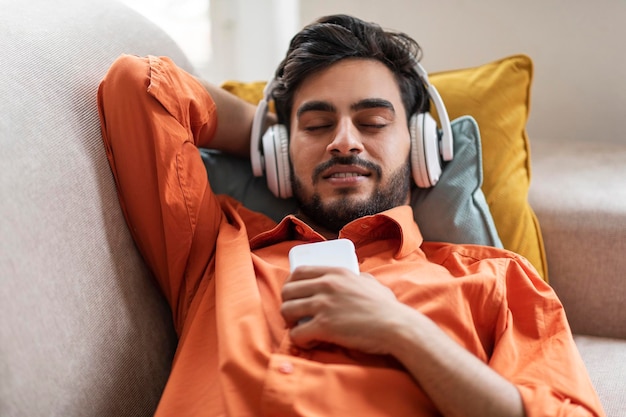 Relaxed guy resting on sofa at home listening to music