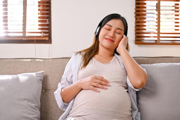 Relaxed and happy Asian pregnant woman listening to music through her headphones