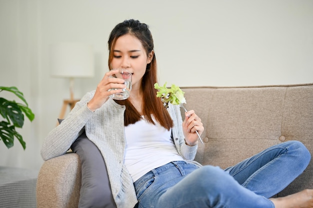 Relaxed and healthy Asian female drinking water and eating her healthy salad