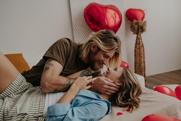 Relaxed loving couple embracing and smiling while lying in bed surrounded with red balloons