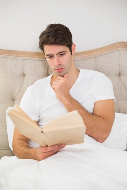 Relaxed man reading book in bed