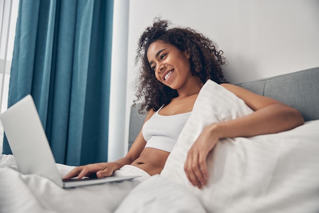 Relaxed pleased beautiful young female freelancer typing on her computer with one hand