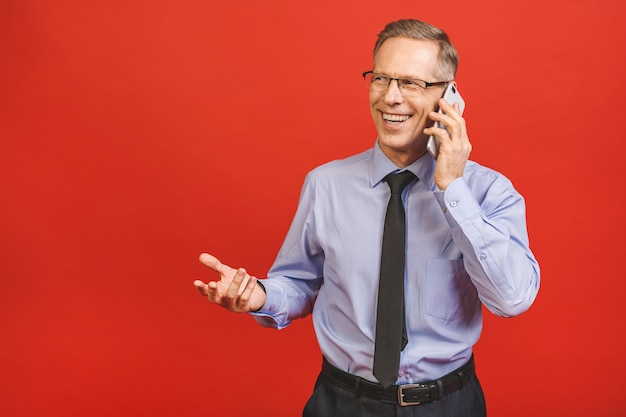 Relaxed senior business man in formal using smartphone isolated on red wall. Portrait of a happy mature businessman using cell phone. Satisfied leader checking mail with copy space.