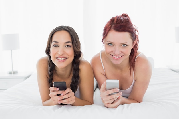 Relaxed smiling female friends text messaging on bed