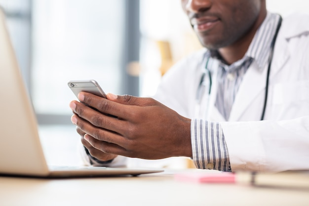 Relaxed student wearing medical uniform and playing with telephone on pause