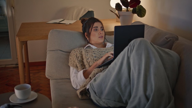 Photo relaxed woman lounging couch looking laptop at evening home environment zoom on