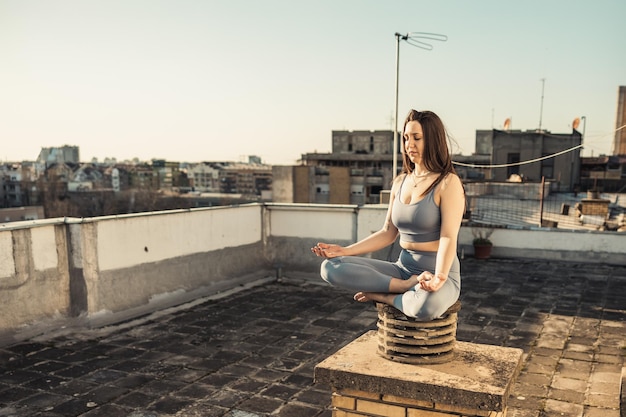 Photo relaxed woman practicing yoga meditating on a rooftop terrace. city buildings in the background.