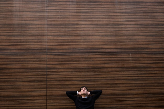 relaxed young handsome man looking up. hands behind head. wood texture wall background. outdoors street. copy space concept