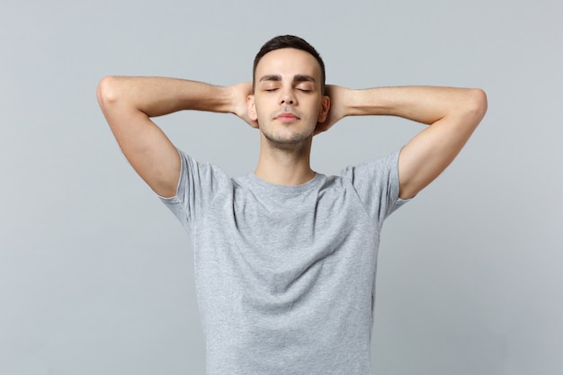 Relaxed young man in casual clothes keeping eyes closed, sleeping with hands behind head 