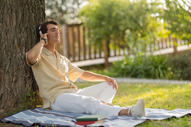 Photo relaxed young man sitting under tree listening to music