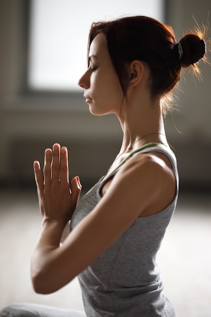 Relaxed young sportswoman doing yoga and meditating in studio.