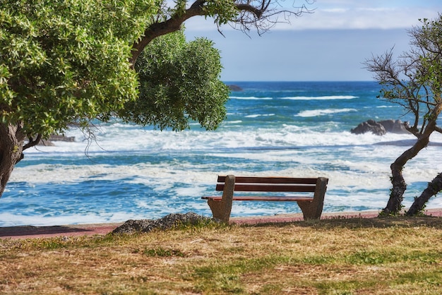 Relaxing bench with sea or ocean view to enjoy calm peaceful or zen beach with waves washing on shore in remote area Scenic seating blue sky and copy space in a coastal park on the promenade