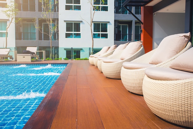 Relaxing rattan chairs with pillows beside swimming pool