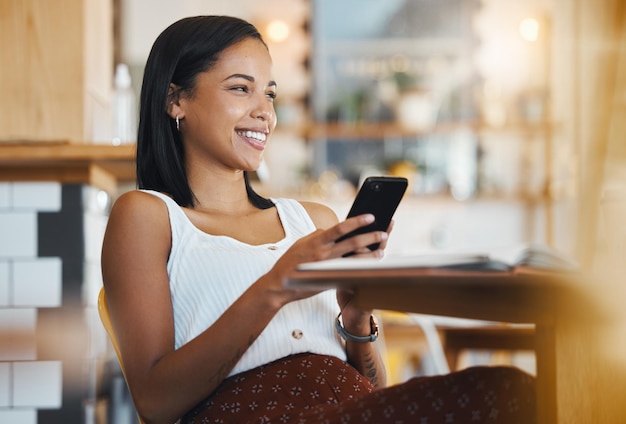 Relaxing texting a message or browsing social media on a phone by a young female student smile in a coffee shop A happy woman thinking and searching the internet or chatting online at a cafe