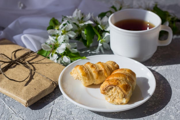 Relaxing time and happiness with cup of tea with among fresh spring flower. Morning tea with a cake on a warm sunny day. Pretty gift box wrapped with simple brown craft paper and decorated with jute.