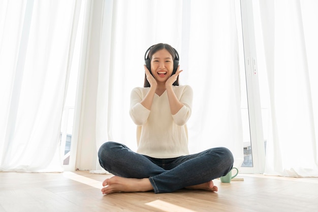 Relex and peaceful asian woman enjoy weekend with music headphone morning sunlight near window home background