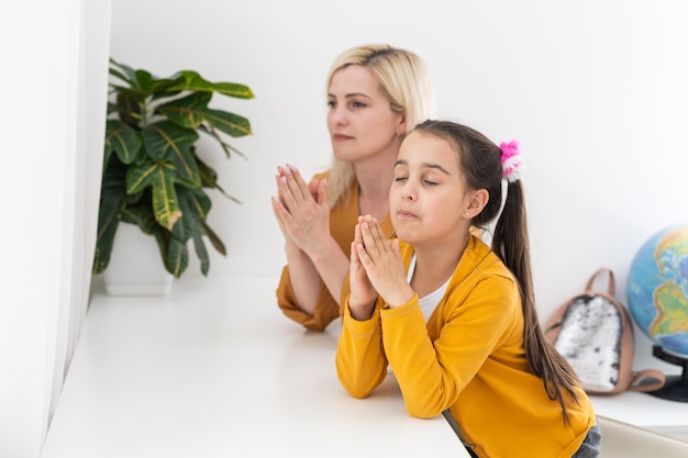 Religious Christian girl and her mother praying at home.