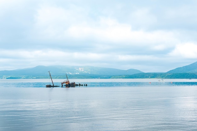 Remains of a sunken ship against the backdrop of a sea bay with foggy mountains in the background