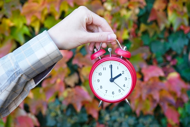 Reminder to switch to winter time A woman holds an alarm clock against the background of autumn leaves