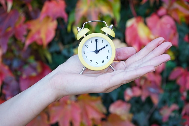 Reminder to switch to winter time A woman holds an alarm clock against the background of autumn leaves