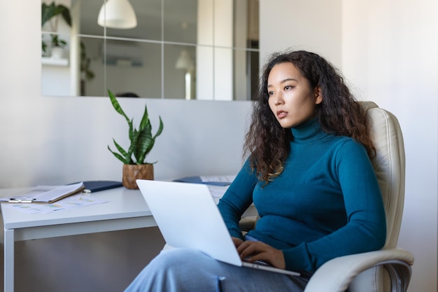 Remote job technology and people concept Focused young Asian business woman with laptop computer and papers working at home office